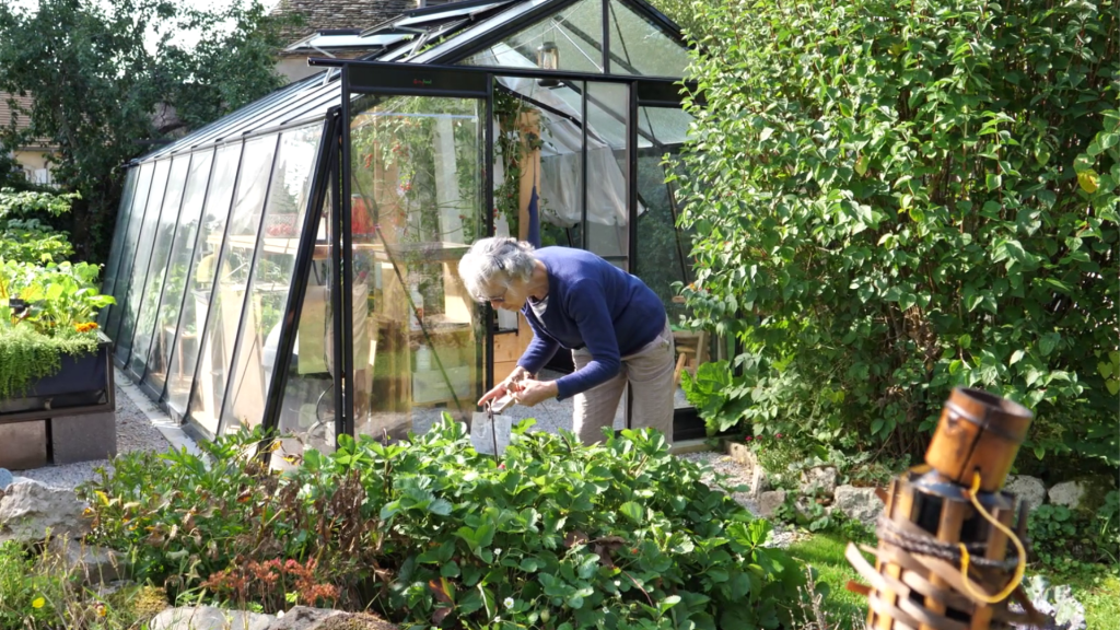 Personne âgée qui jardine aux abords de sa serre